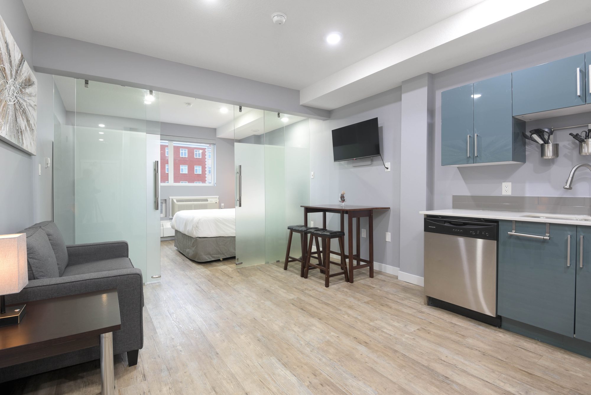 Open living area with sofa, kitchen with teal cabinets, and view into the bedroom