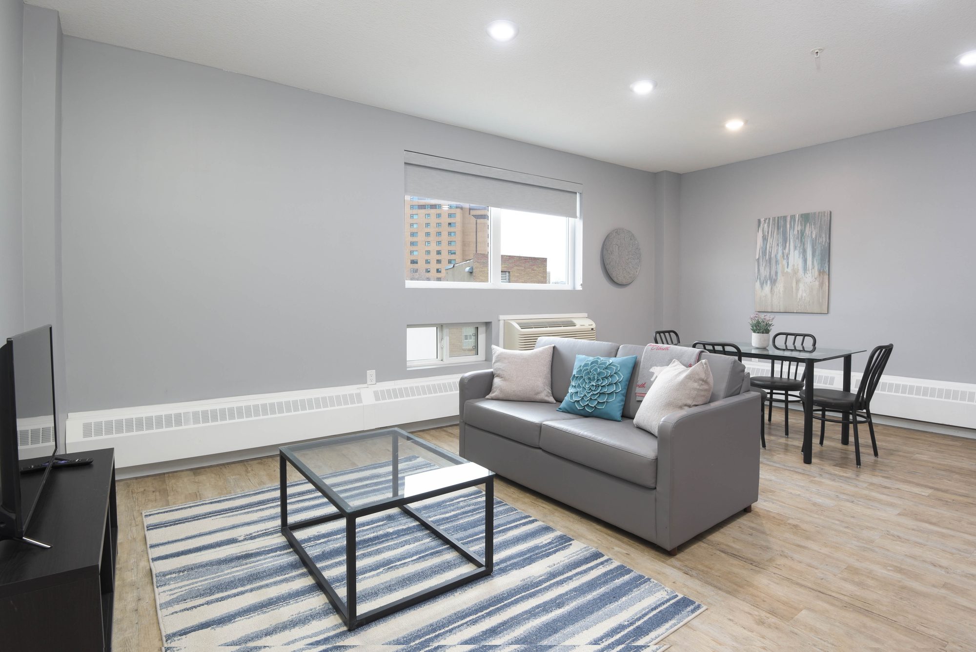 Two bedroom living room with sofa, patterned rug, glass coffee table, and dining table